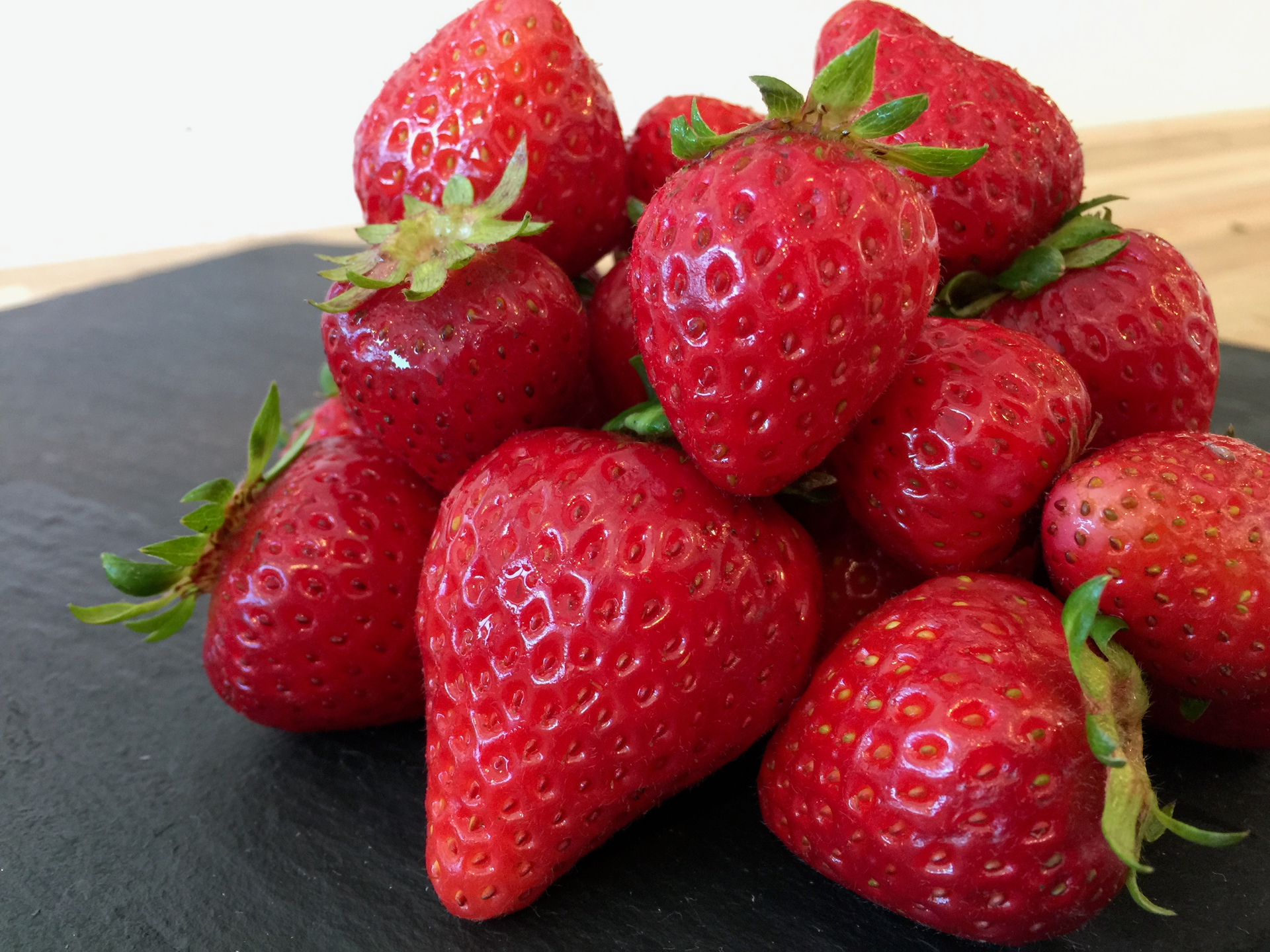 A pile of fresh strawberries sits atop a black board.